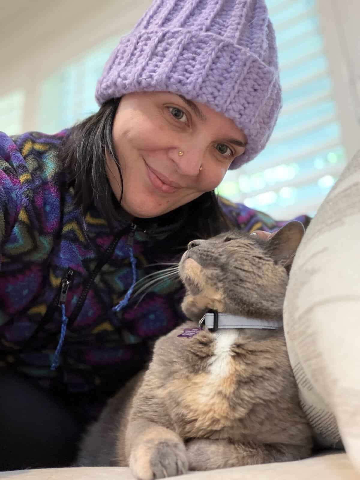 Close-up of woman with purple knit hat cuddling her tabby cat.